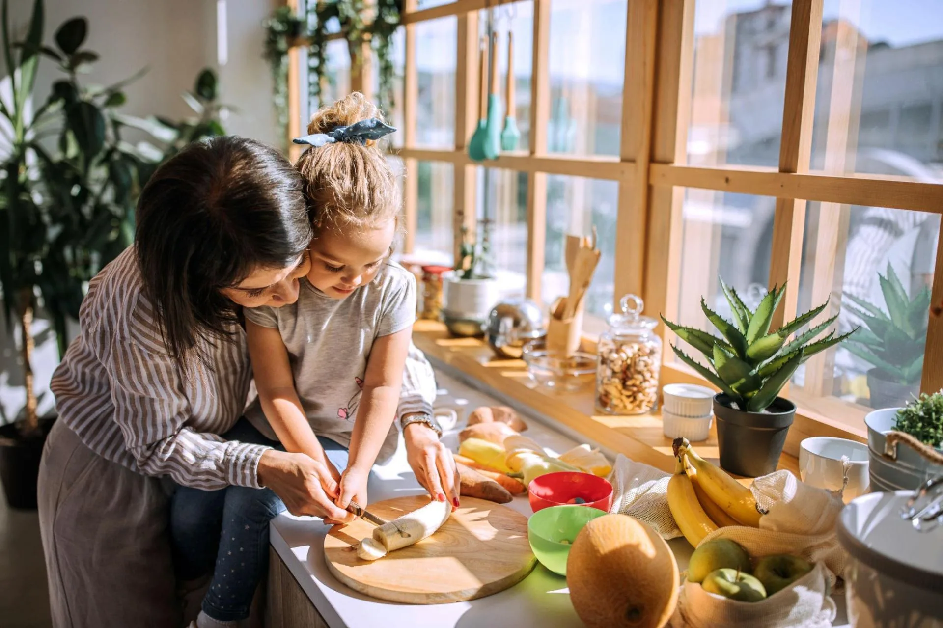 A mother and daughter slicing banana together in a bright home kitchen
